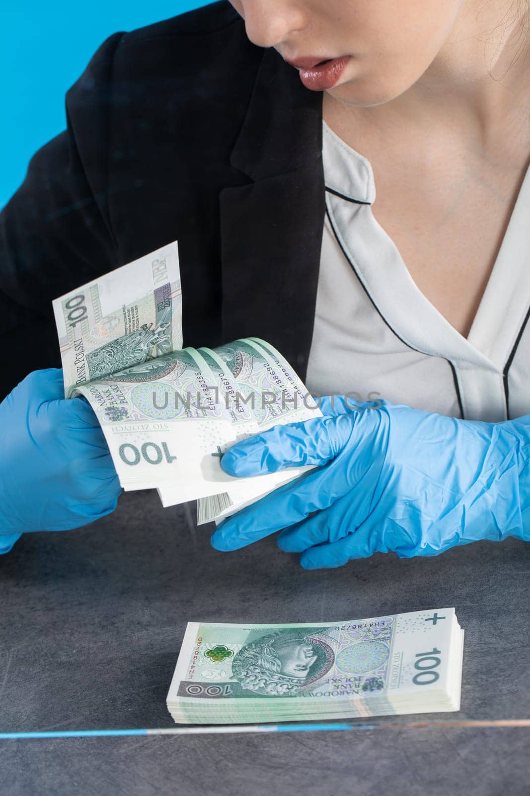 Hand counting banknotes by a young woman at the cashier's window in a large banking branch.