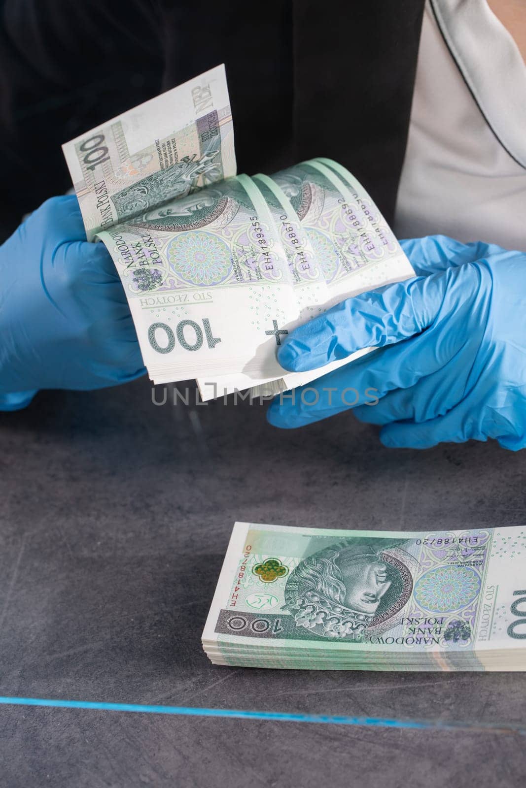 Hand counting banknotes by a young woman at the cashier's window in a large banking branch.