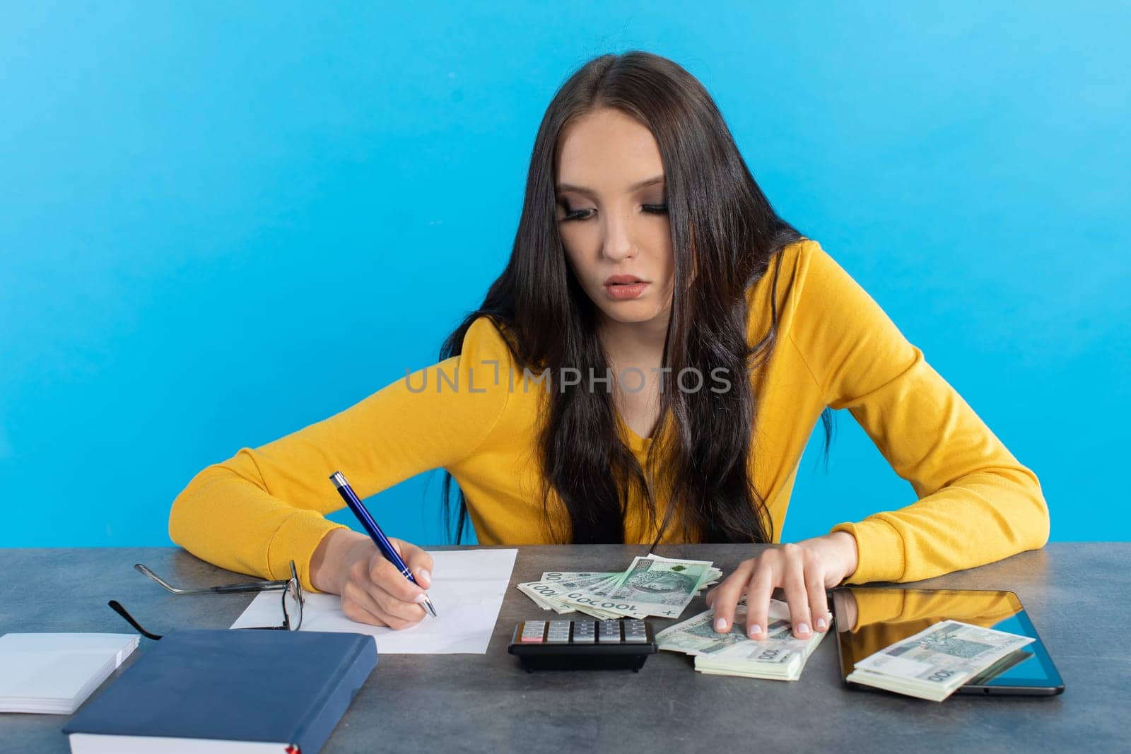 While counting money, a young woman uses a calculator and a tablet to check the stock exchange.