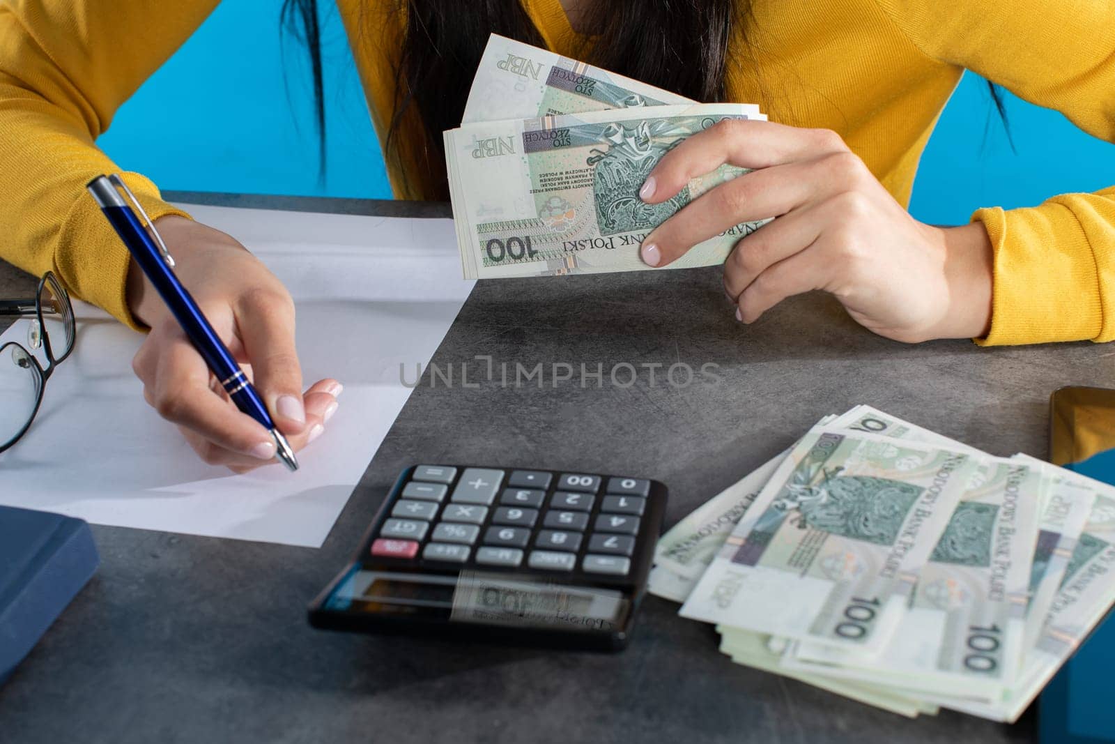On the desk lies a calculator, tablet and a stack of paper banknotes, which the young woman counts.