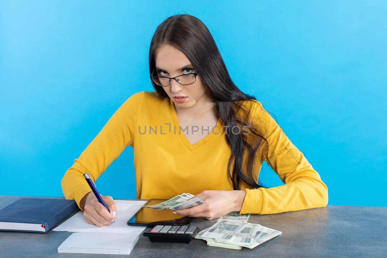 While counting money, a young woman uses a calculator and a tablet to check the stock exchange.