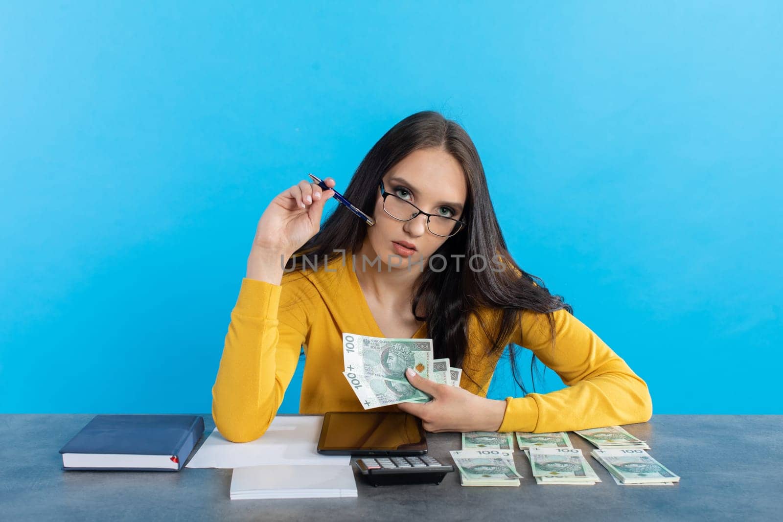While counting money, a young woman uses a calculator and a tablet to check the stock exchange.