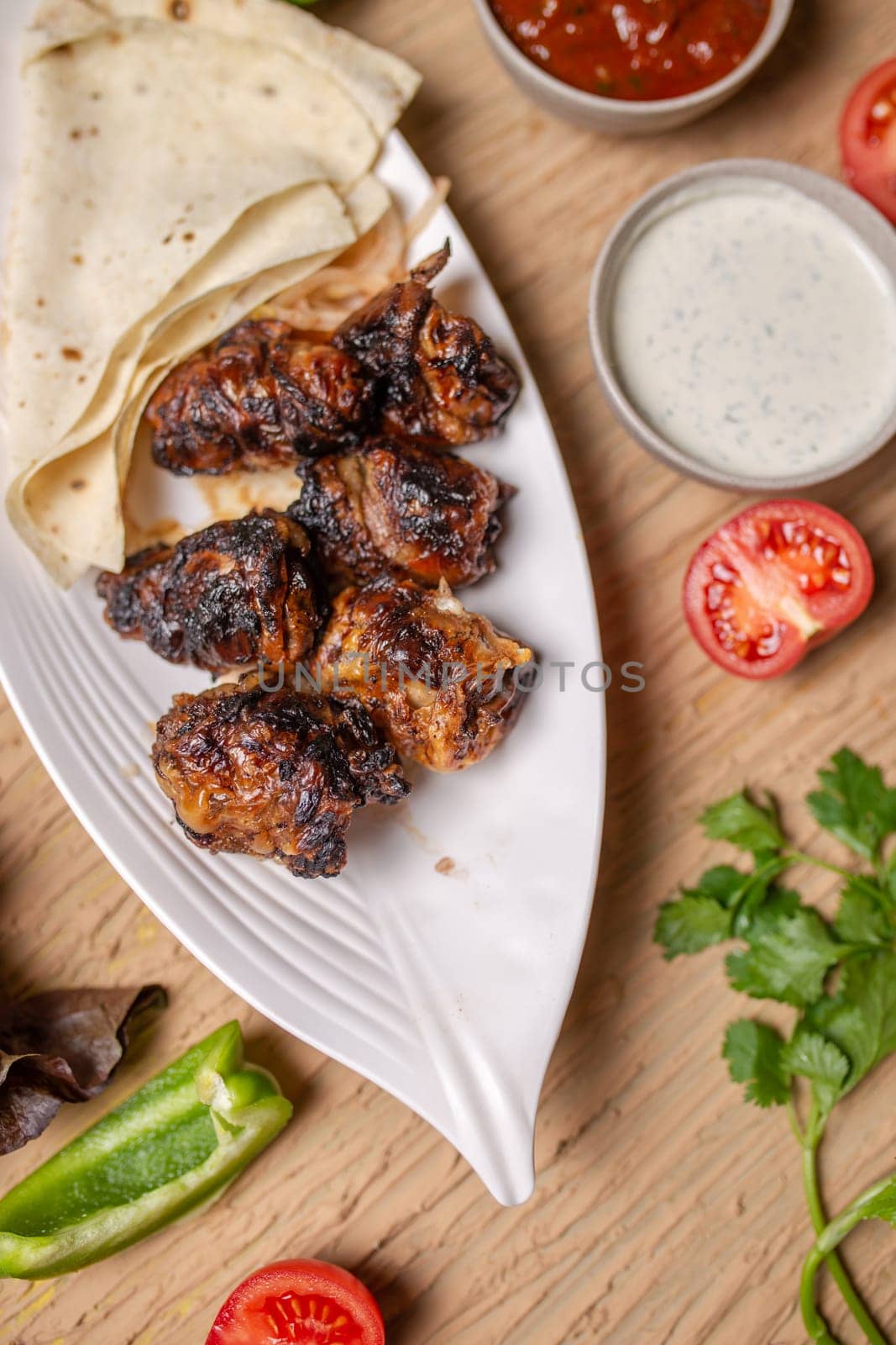 liver kebab with pita bread on a white plate with vegetables and herbs by Pukhovskiy