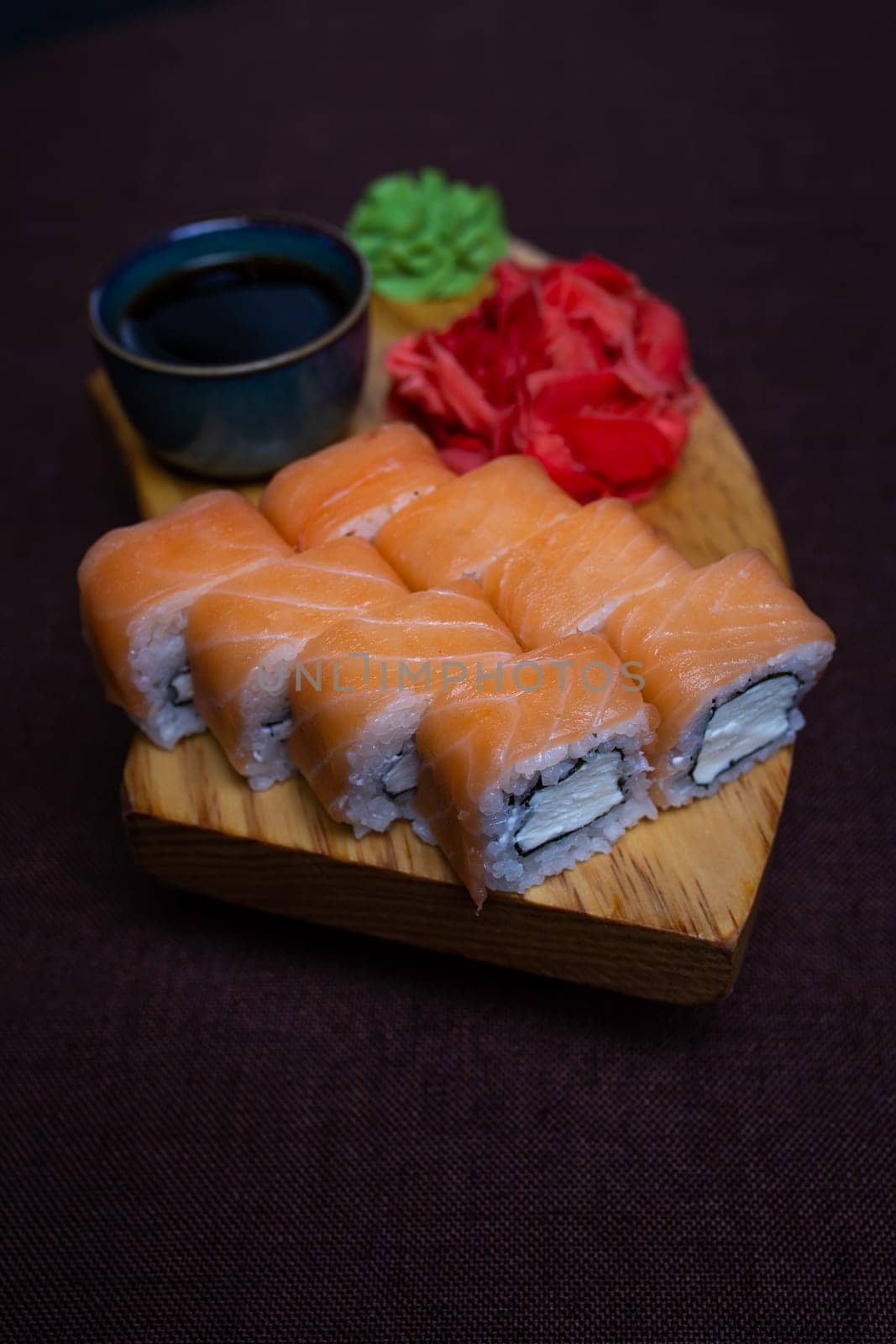 Closeup of traditional Japanese sushi rolls, wasabi paste, and pickled ginger on a wooden plate over dark background