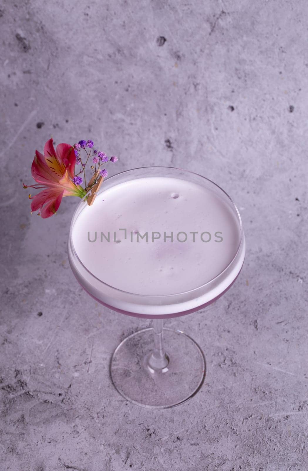 Elegant pink cocktail in a glass with a floral side dish on a gray background top view by Pukhovskiy