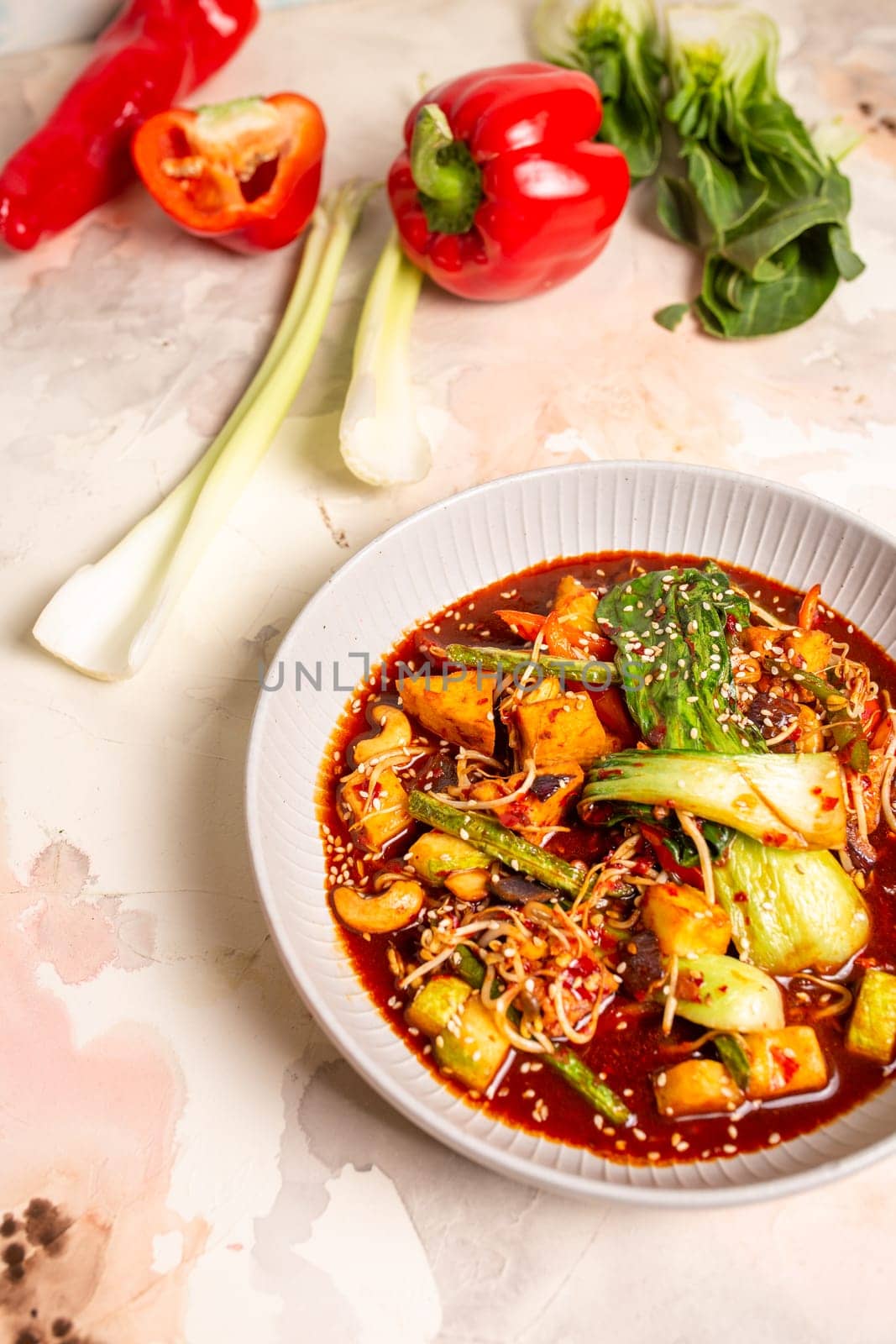 Red curry with veggies, tofu on a white background. Made with coconut milk, red curry paste, garnished with sesame seeds.