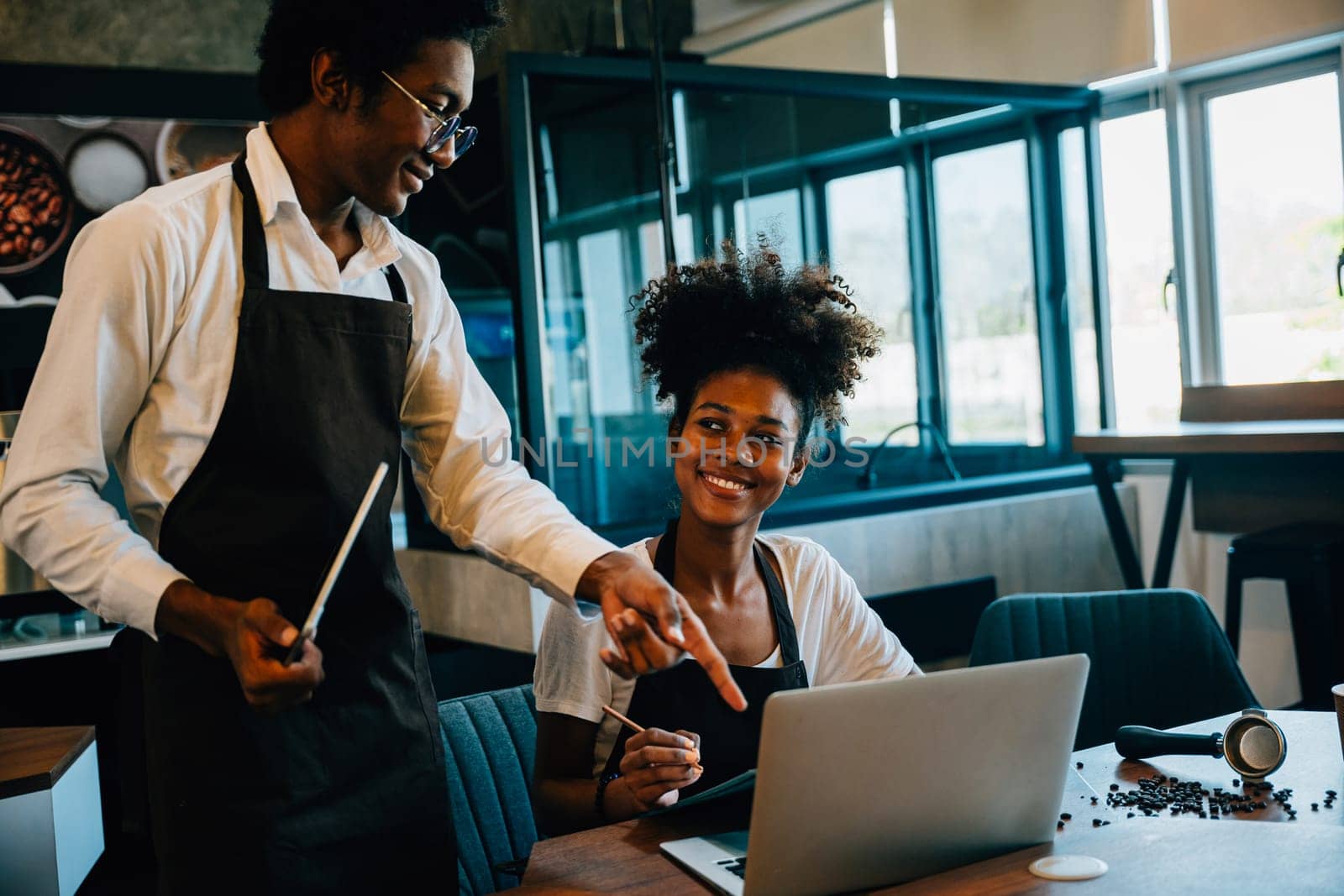 Cafe owners a black barista and owner plan supply orders on laptop. Discussing work schedule menu teamwork in coffee shop aiming for business success financial planning.