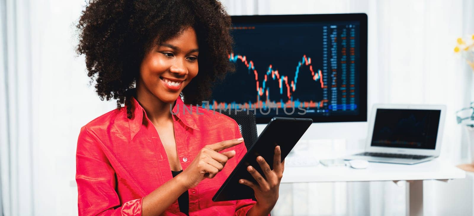 Analytical young African American businesswoman, a specialist in successful stock exchange trading, against dynamic data graph displaying marketing trend analysis on screen. Tastemaker.