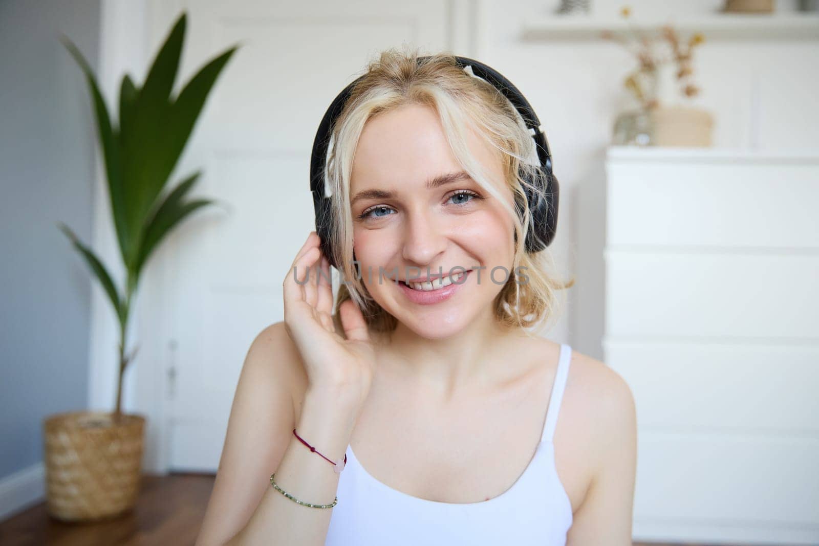 Portrait of good-looking young blond woman in wireless headphones, listens to podcast or favourite song, enjoys music in new earphones by Benzoix