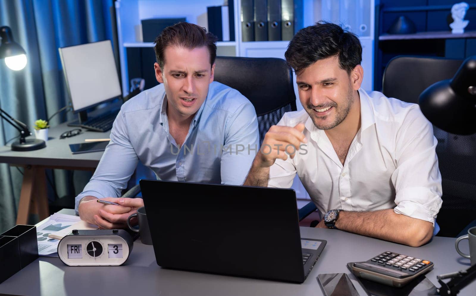 Business partners focusing on laptop, working together with good relation at night time in modern office, analyzing on creative project at blue neon decorative room. Concept of brainstorm. Sellable.