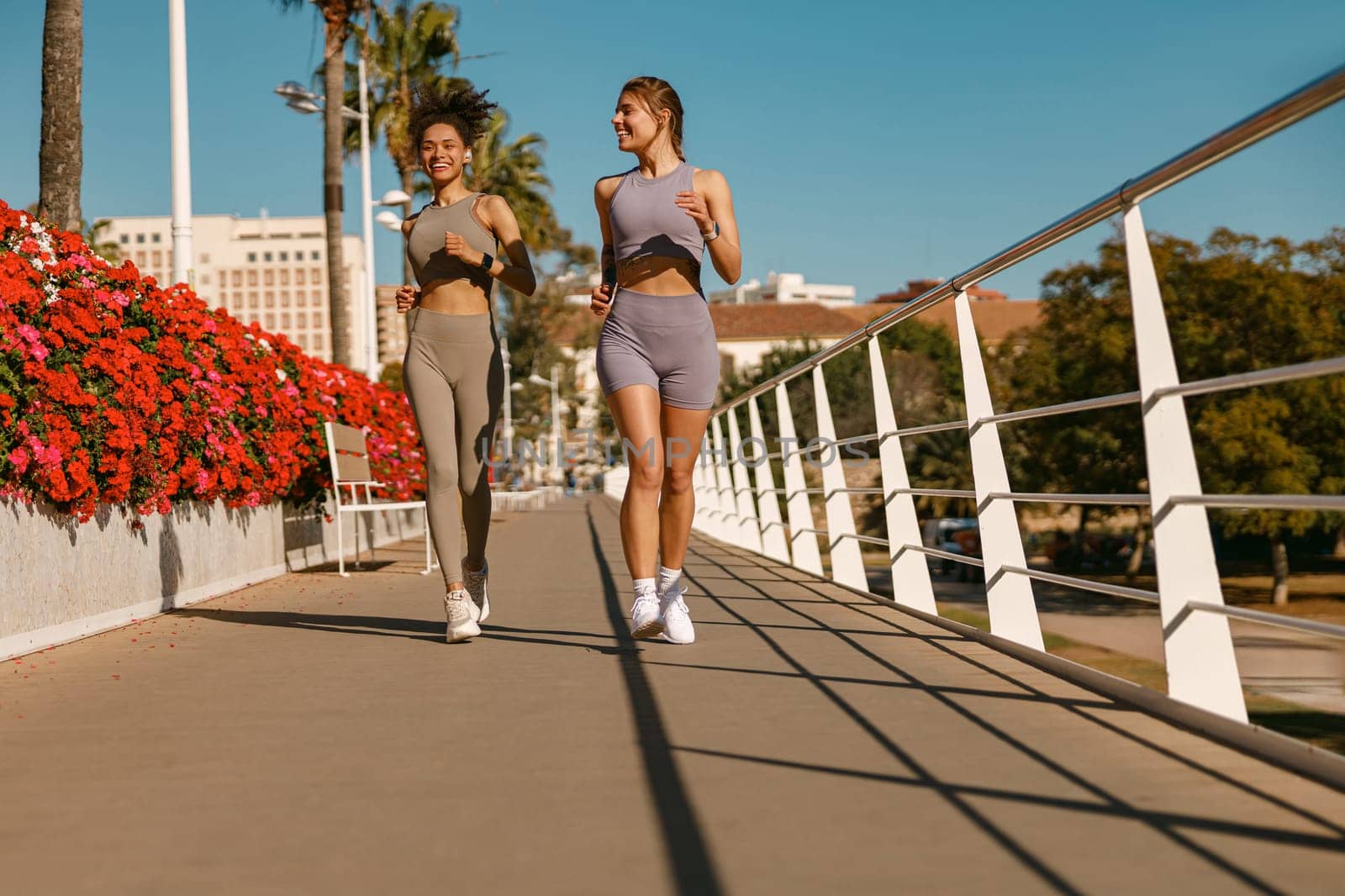 Two young women in sportswear are running on modern buildings background. Active lifestyle concept