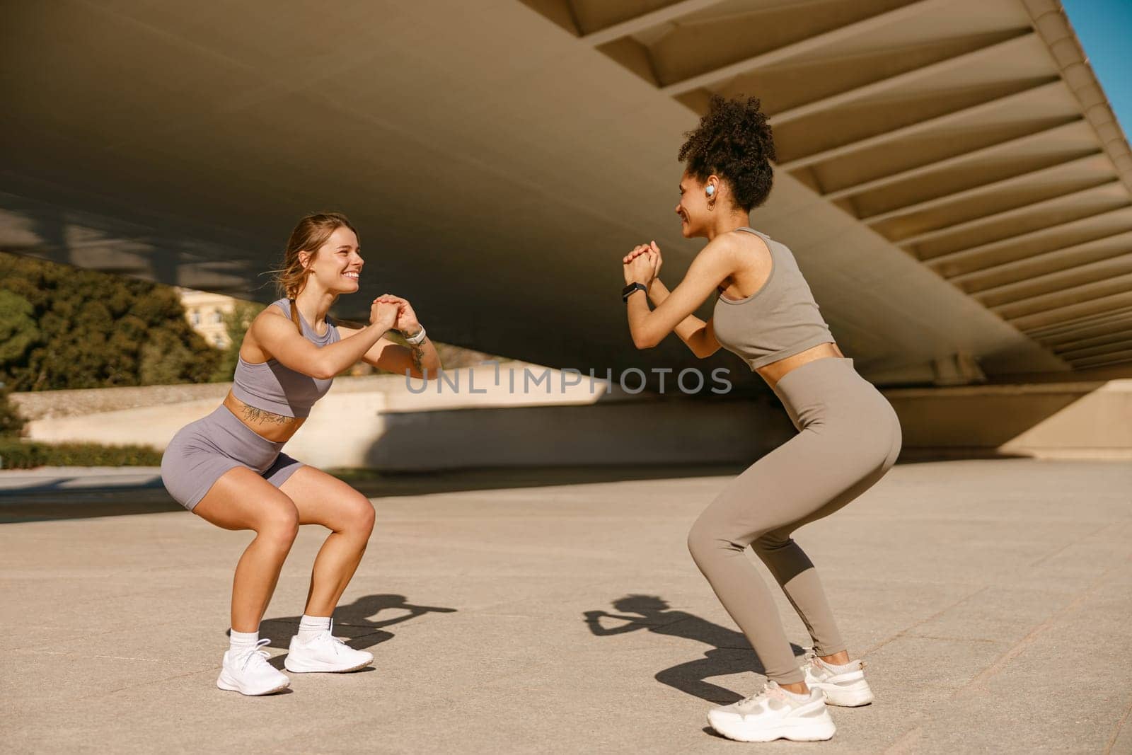 Two smiling fit women doing workout and squatting together outdoors. Active lifestyle concept by Yaroslav_astakhov