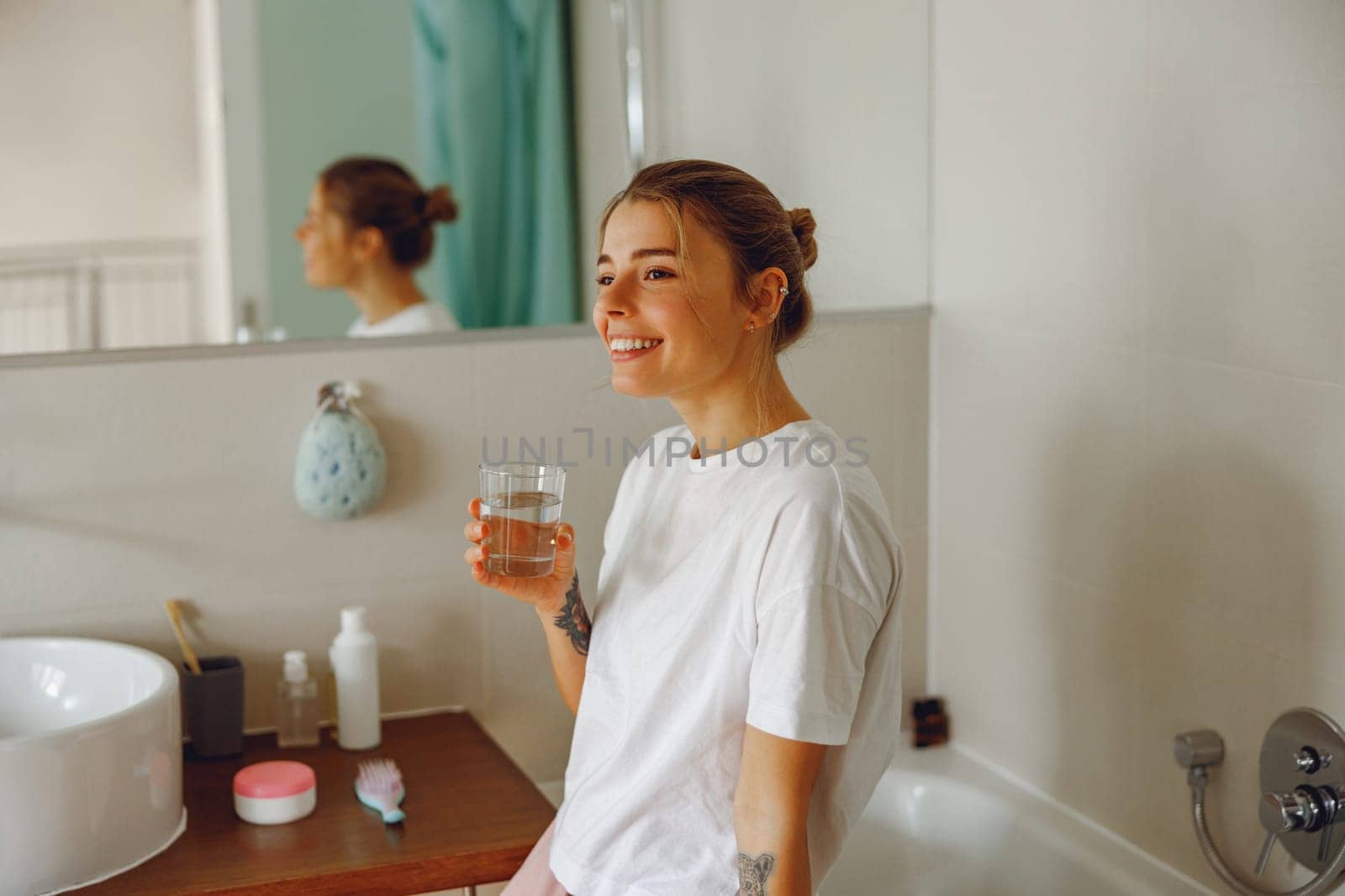 Young beautiful woman drinking glass of water in the bathroom at home. Beauty treatment by Yaroslav_astakhov