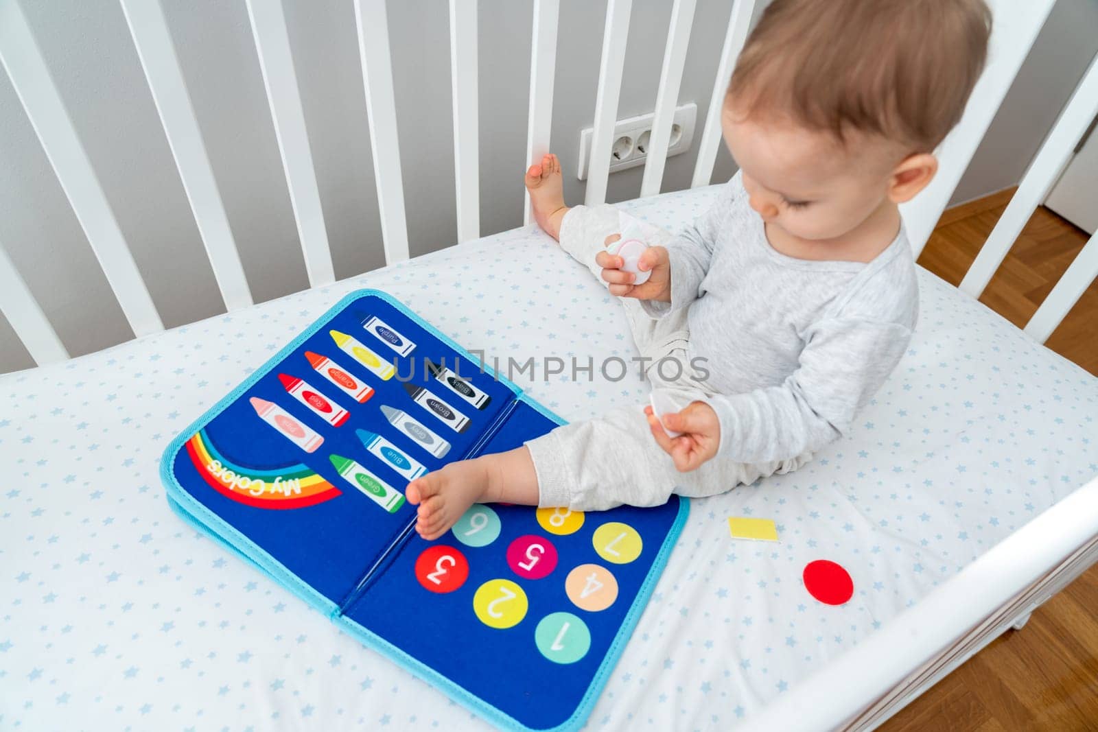 Baby playing with busy book sitting in crib. Concept of smart books and modern toys by Mariakray