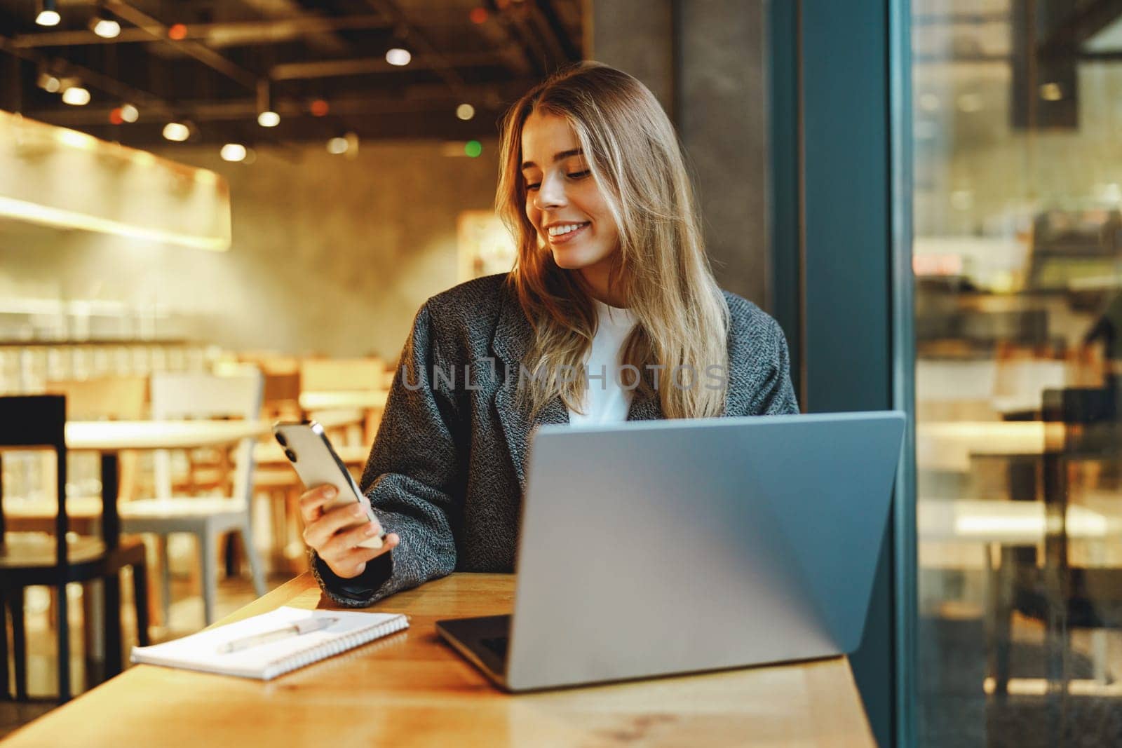 Smiling woman manager is using phone and work on laptop outside of office. Distance work concept