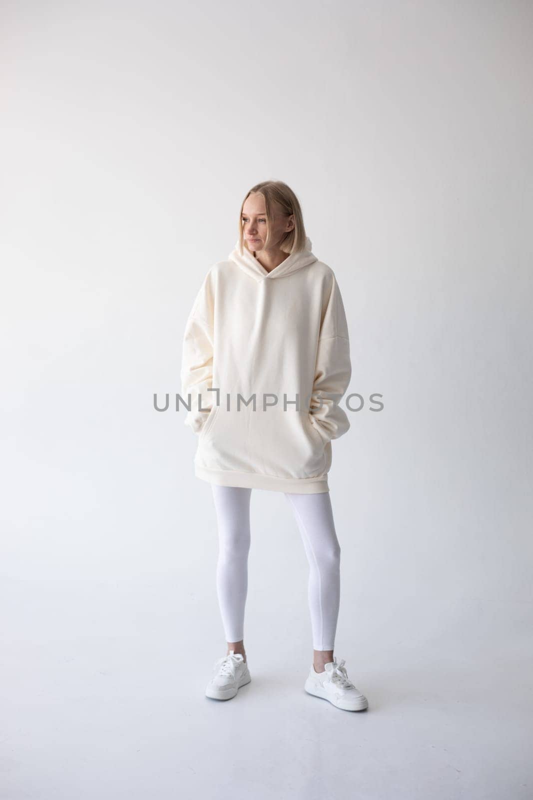 Blonde girl in a white hoodie and tights posing on a white background. High quality photo