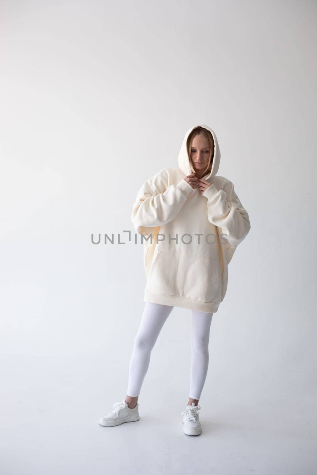 Blonde girl in a white hoodie and tights posing on a white background by Freeman_Studio