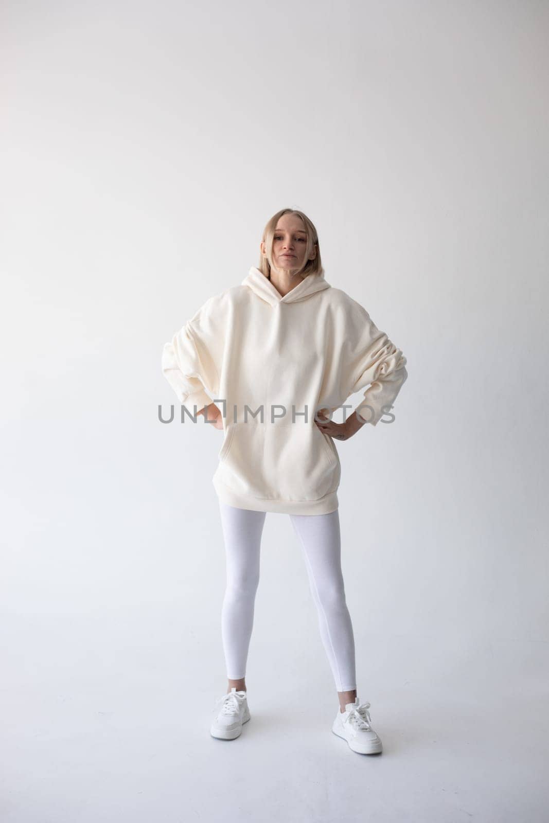 Blonde girl in a white hoodie and tights posing on a white background. High quality photo