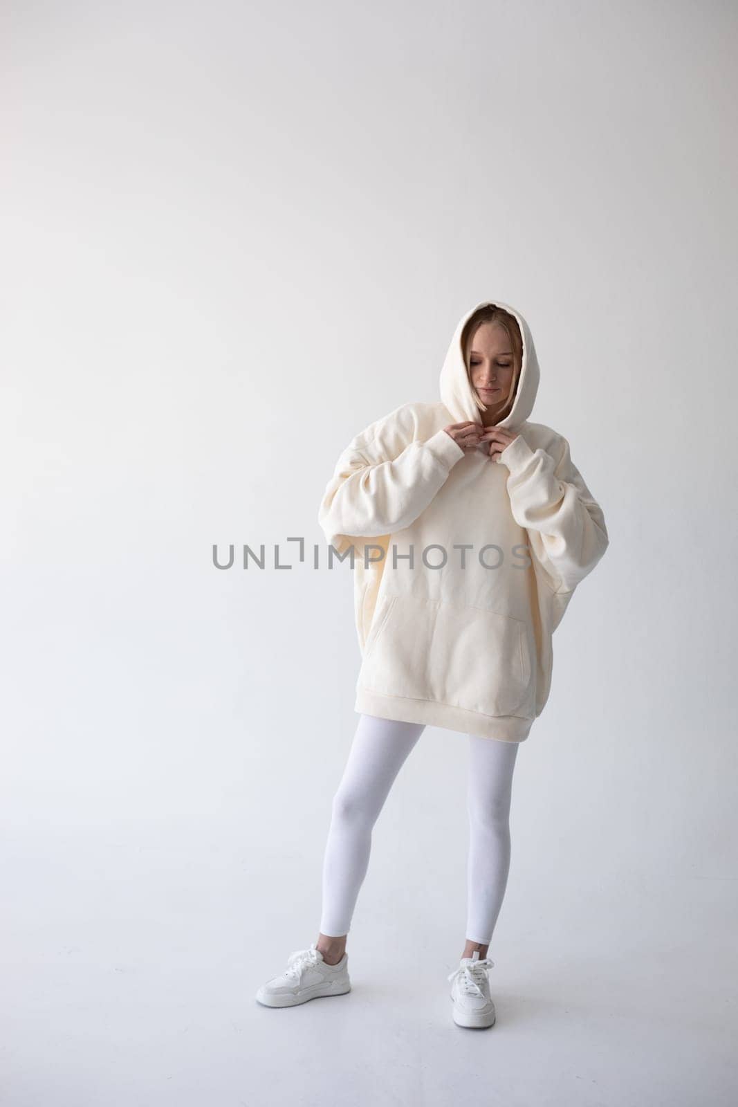 Blonde girl in a white hoodie and tights posing on a white background by Freeman_Studio