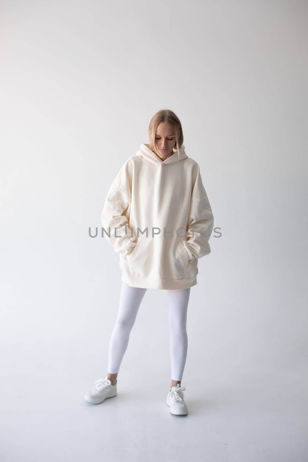 Blonde girl in a white hoodie and tights posing on a white background. High quality photo