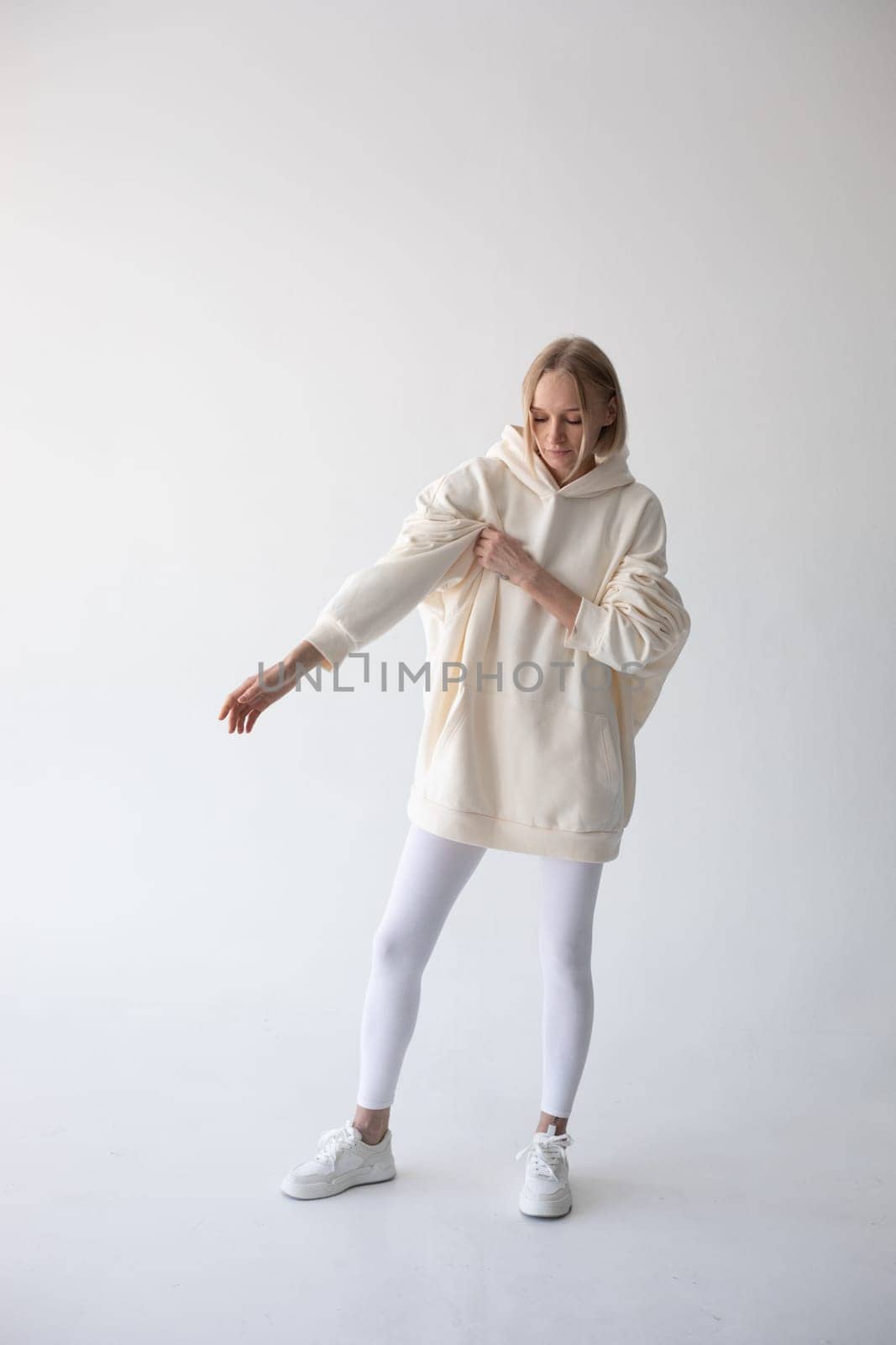 Blonde girl in a white hoodie and tights posing on a white background by Freeman_Studio