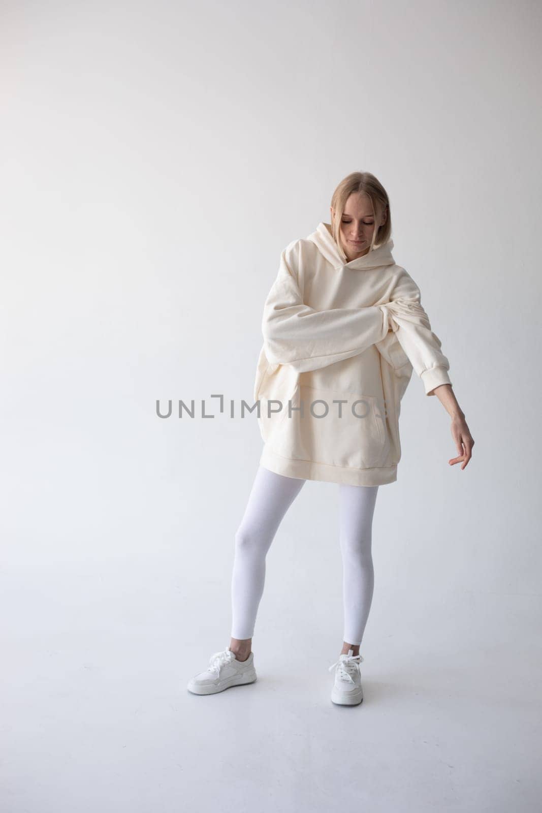 Blonde girl in a white hoodie and tights posing on a white background by Freeman_Studio