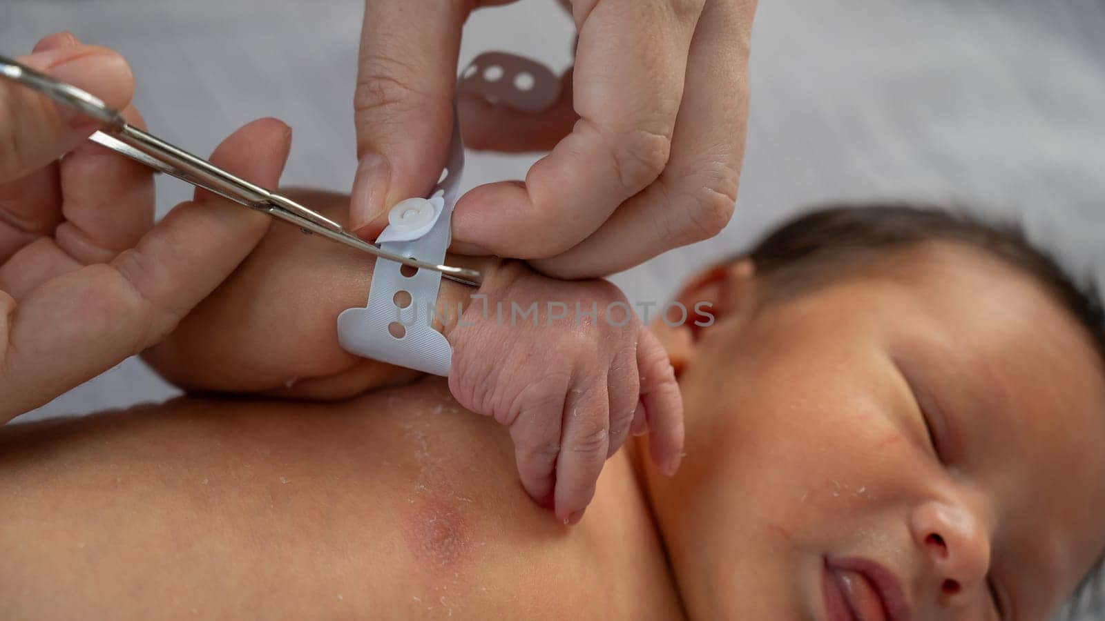 A woman cuts a tag from a newborn boy's hand with nail scissors. Close-up of hands