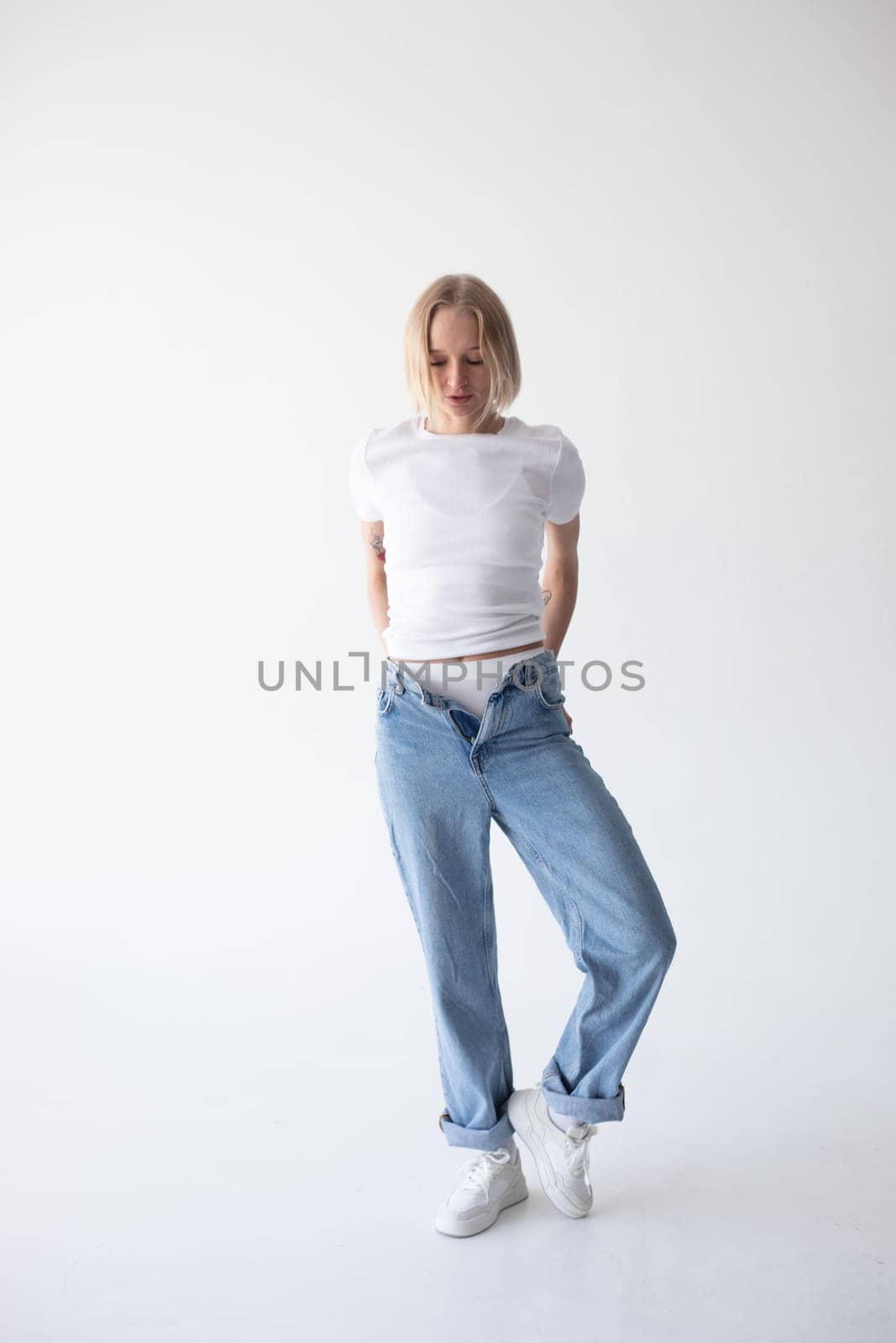 Beautiful blonde girl in a white T-shirt and blue jeans and sneakers posing on a white background. High quality photo