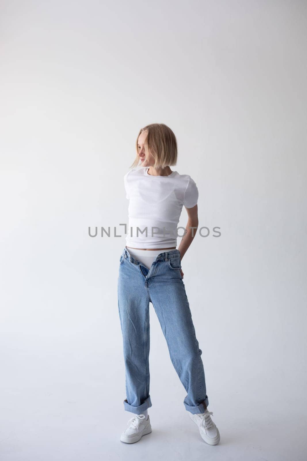 Beautiful blonde girl in a white T-shirt and blue jeans and sneakers posing on a white background. High quality photo