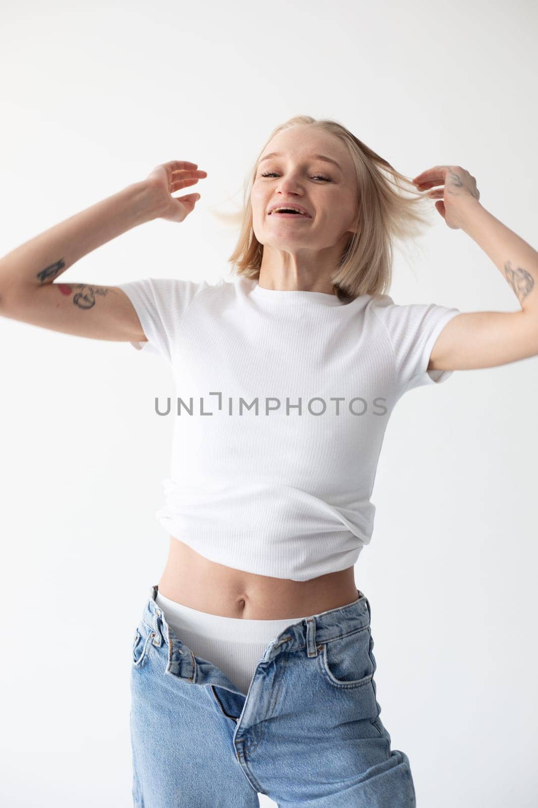 Beautiful blonde girl in a white T-shirt and blue jeans and sneakers posing on a white background. High quality photo