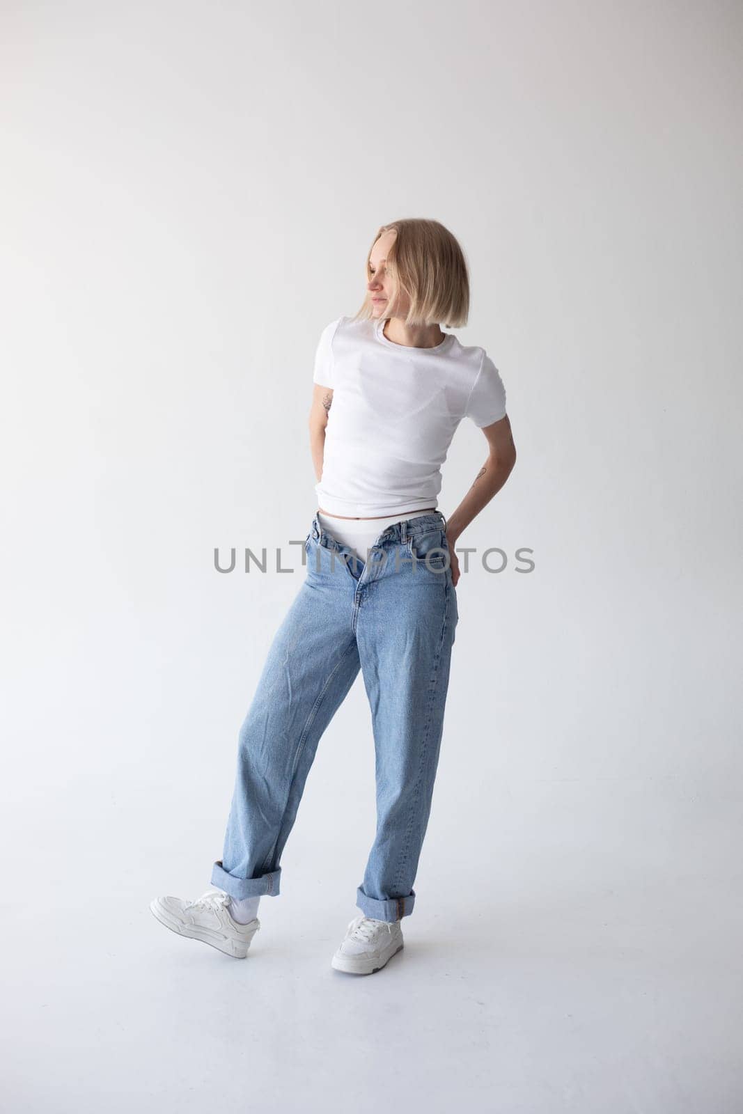 Beautiful blonde girl in a white T-shirt and blue jeans and sneakers posing on a white background. High quality photo