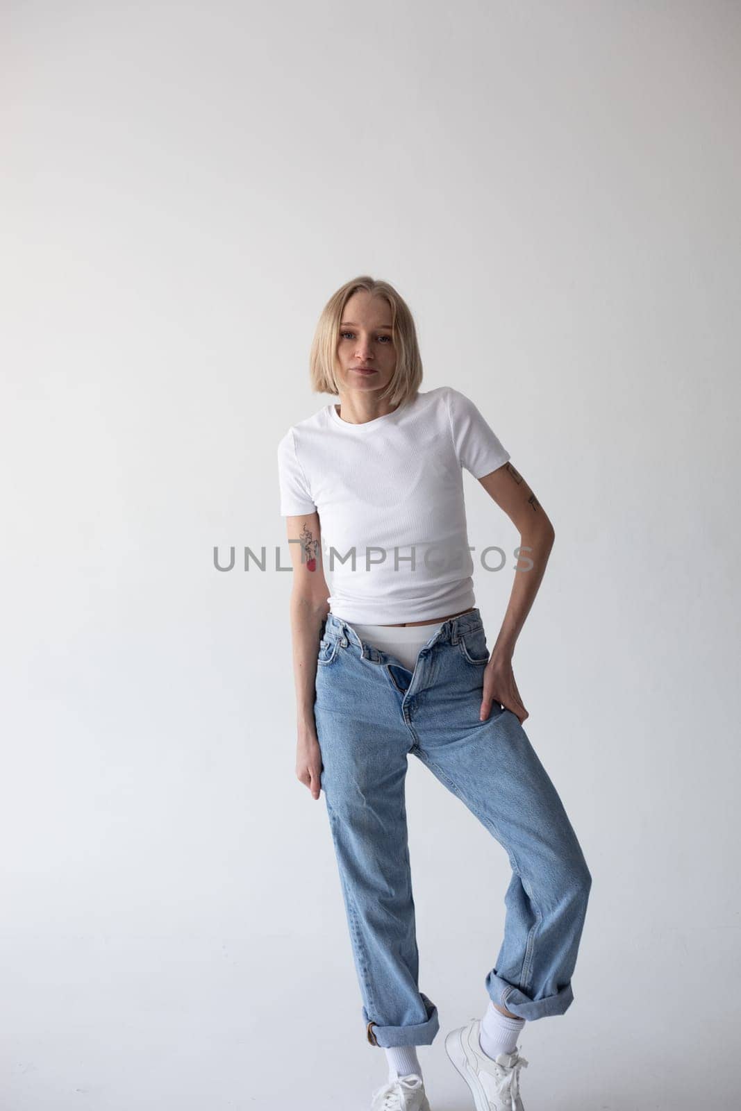 Beautiful blonde girl in a white T-shirt and blue jeans and sneakers posing on a white background. High quality photo