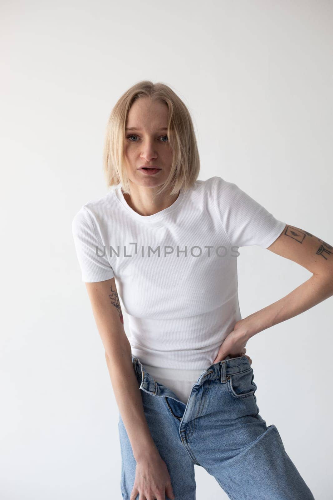 Beautiful blonde girl in a white T-shirt and blue jeans and sneakers posing on a white background. High quality photo