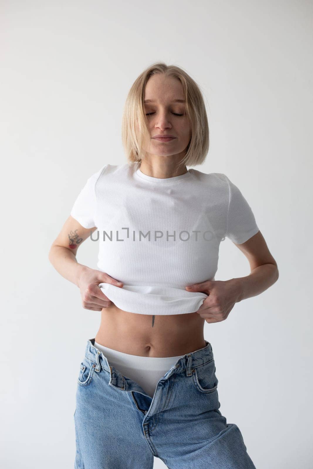Beautiful blonde girl in a white T-shirt and blue jeans and sneakers posing on a white background. High quality photo
