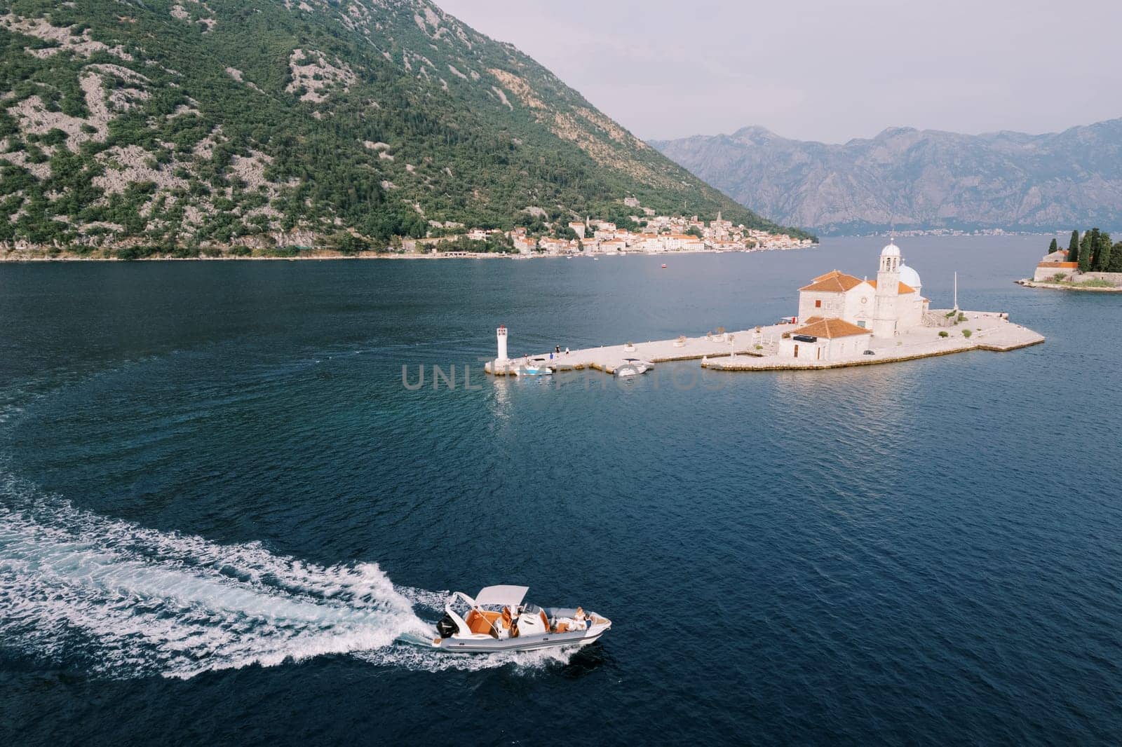 Motorboat sails on the sea past the Church of Our Lady on the Rocks of the island of Gospa od Skrpjela. Montenegro. Drone by Nadtochiy