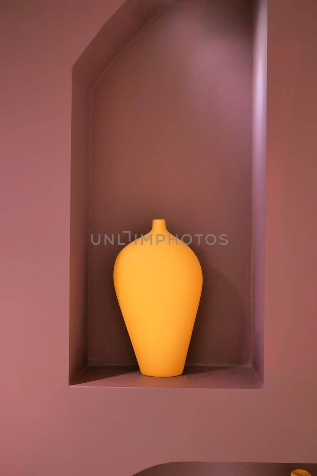 A wooden artifact, a yellow vase, sits in a niche on a purple wall,