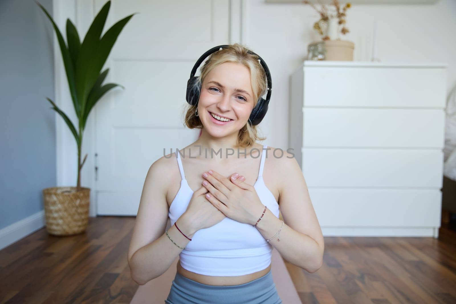 Portrait of young happy woman in headphones, looking with relaxed, friendly face expression, holding hands on her chest and smiling.