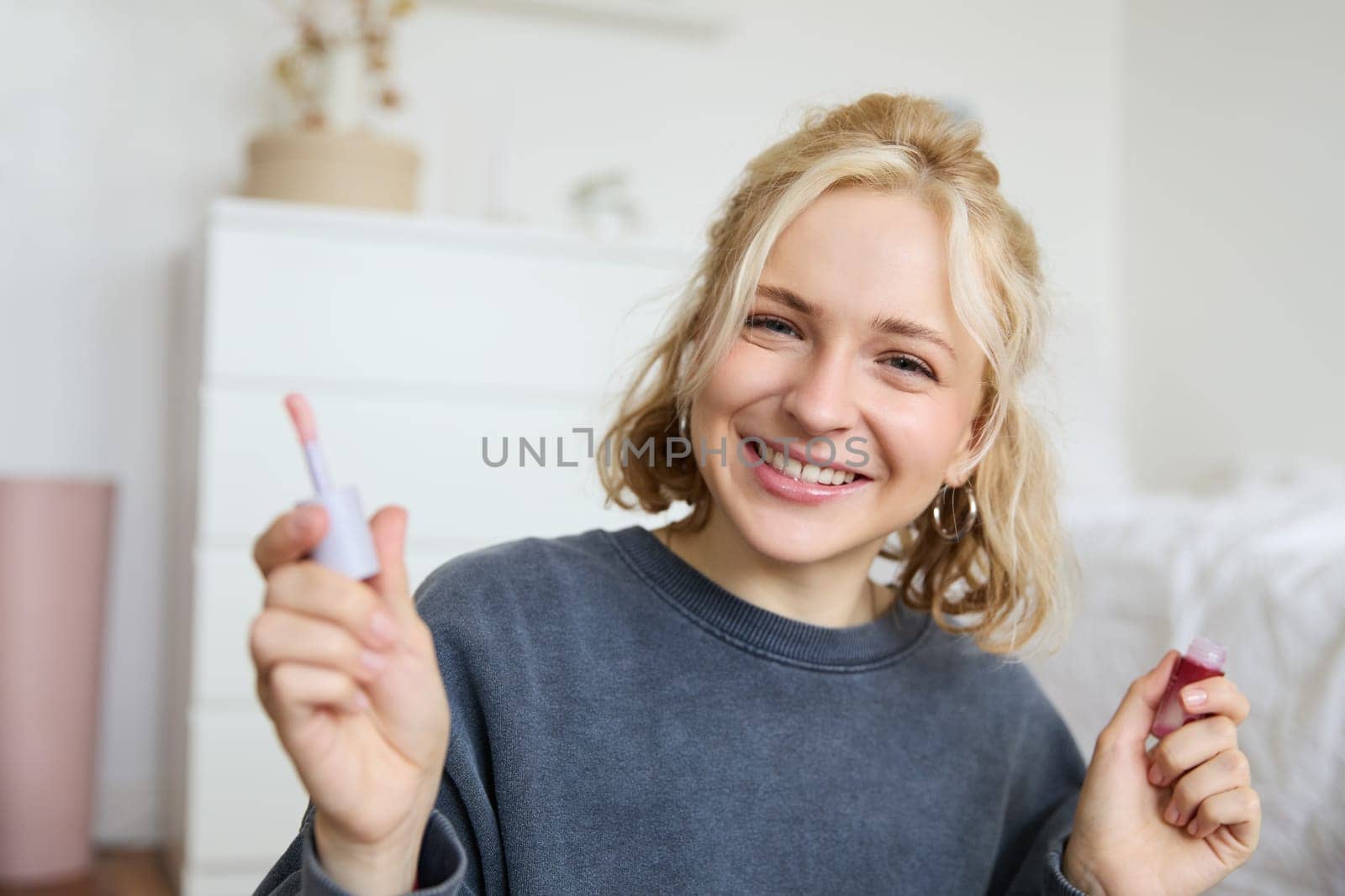 Close up portrait of woman recording a video of herself, holding beauty product, recommending lip gloss, content maker advertising makeup on her blog, smiling at camera.