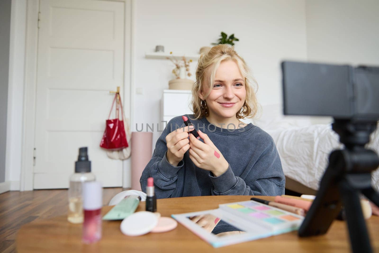 Portrait of young content maker, woman blogger recording a video on digital camera, showing lipstick colour to her followers, creating lifestyle vlog for social media account.