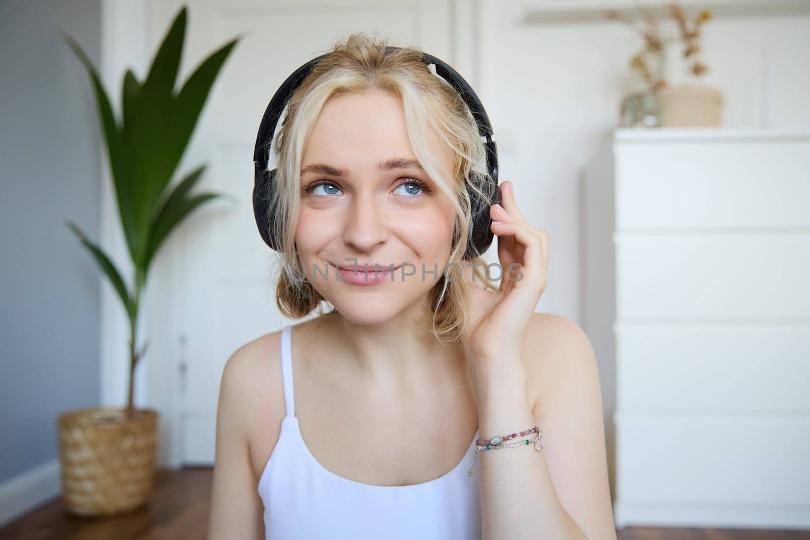 Portrait of good-looking young blond woman in wireless headphones, listens to podcast or favourite song, enjoys music in new earphones by Benzoix