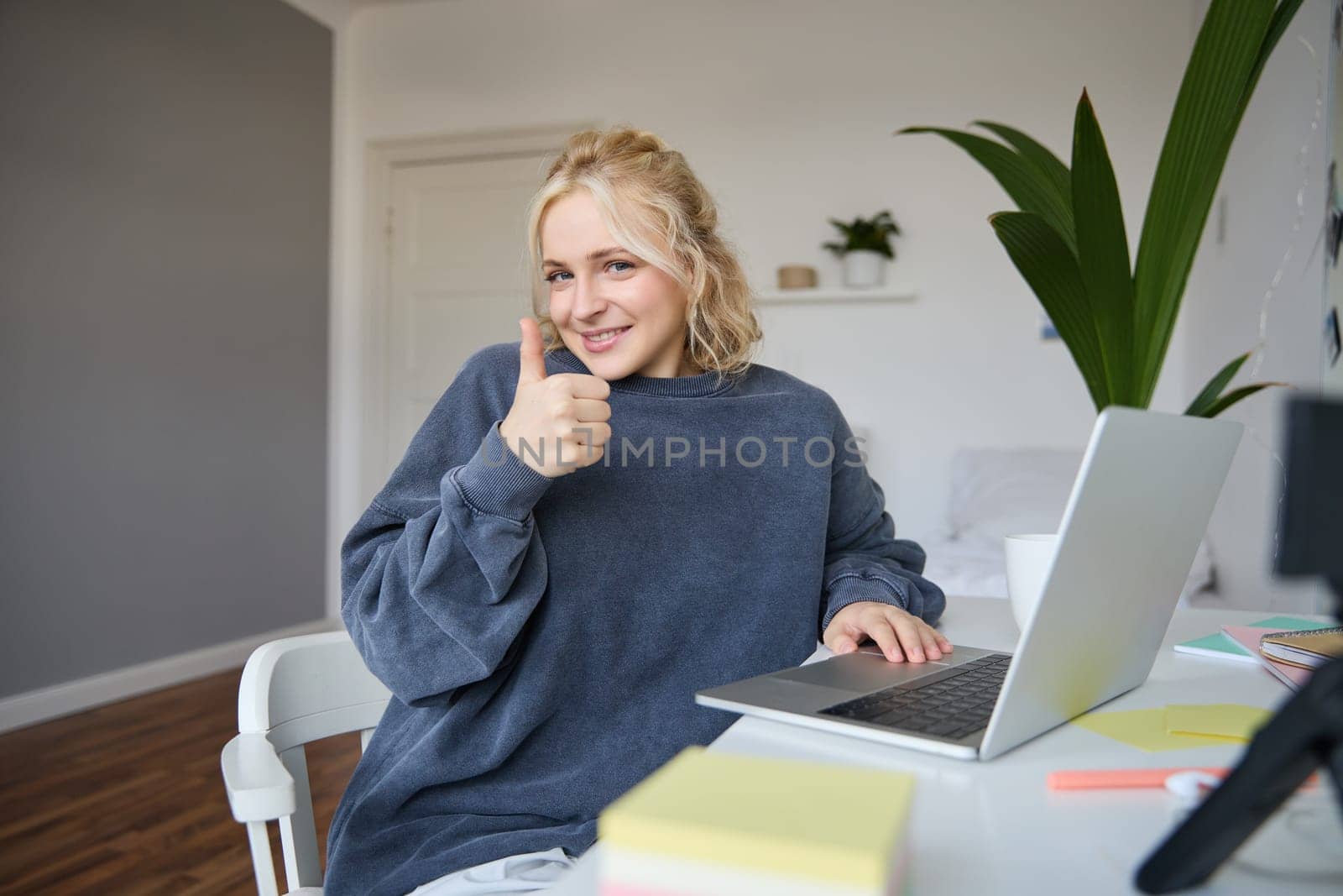Portrait of smiling young blond woman, girl student studying from home, using online academy, doing course in internet, using laptop, showing thumbs up. Concept of distance learning.