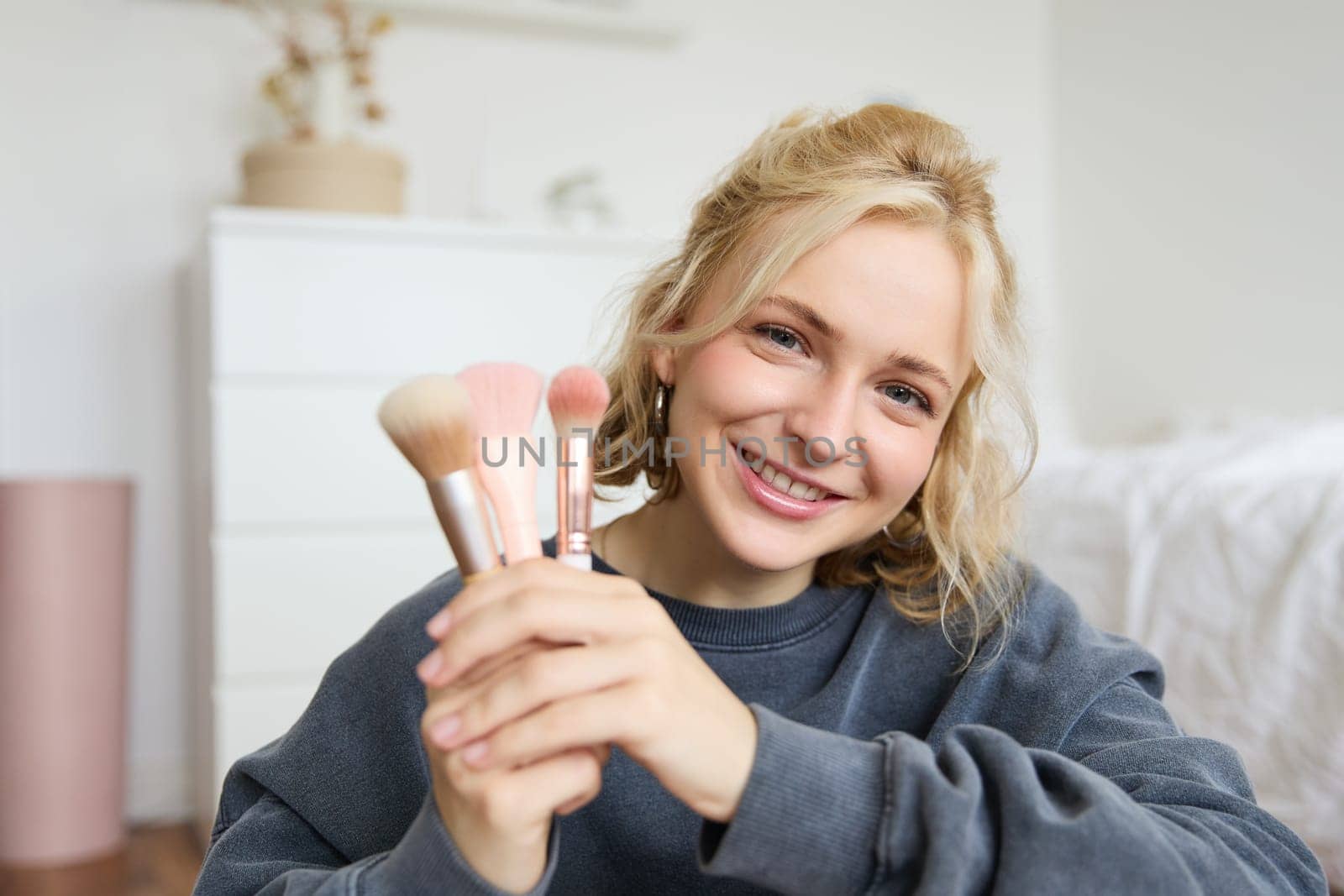 Close up portrait of cute teen girl showing her beauty makeup brushes, smiling and looking at camera.