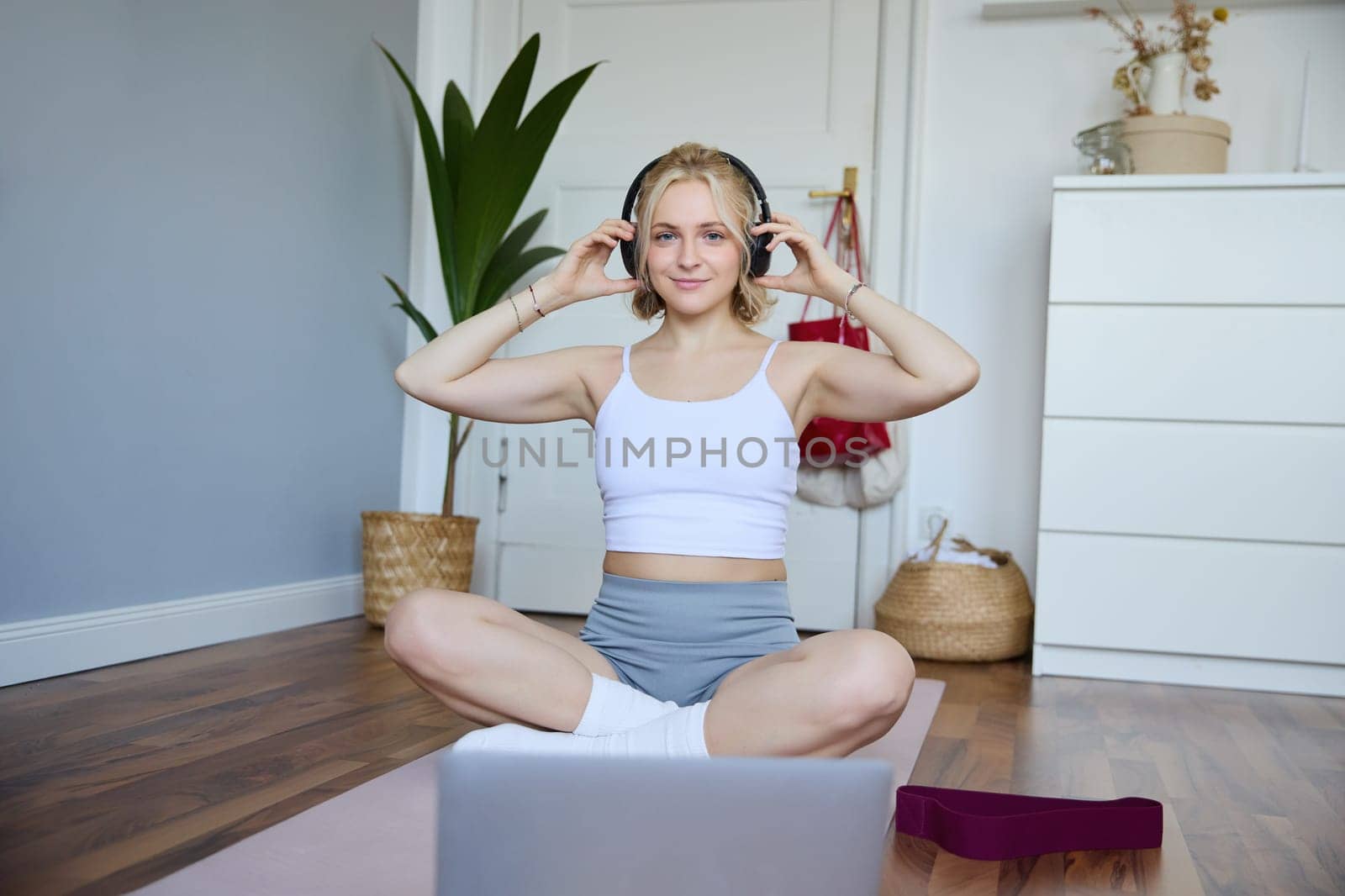 Portrait of young fitness girl, woman workout at home, listens to fitness instructor in wireless headphones, follows exercises on laptop.