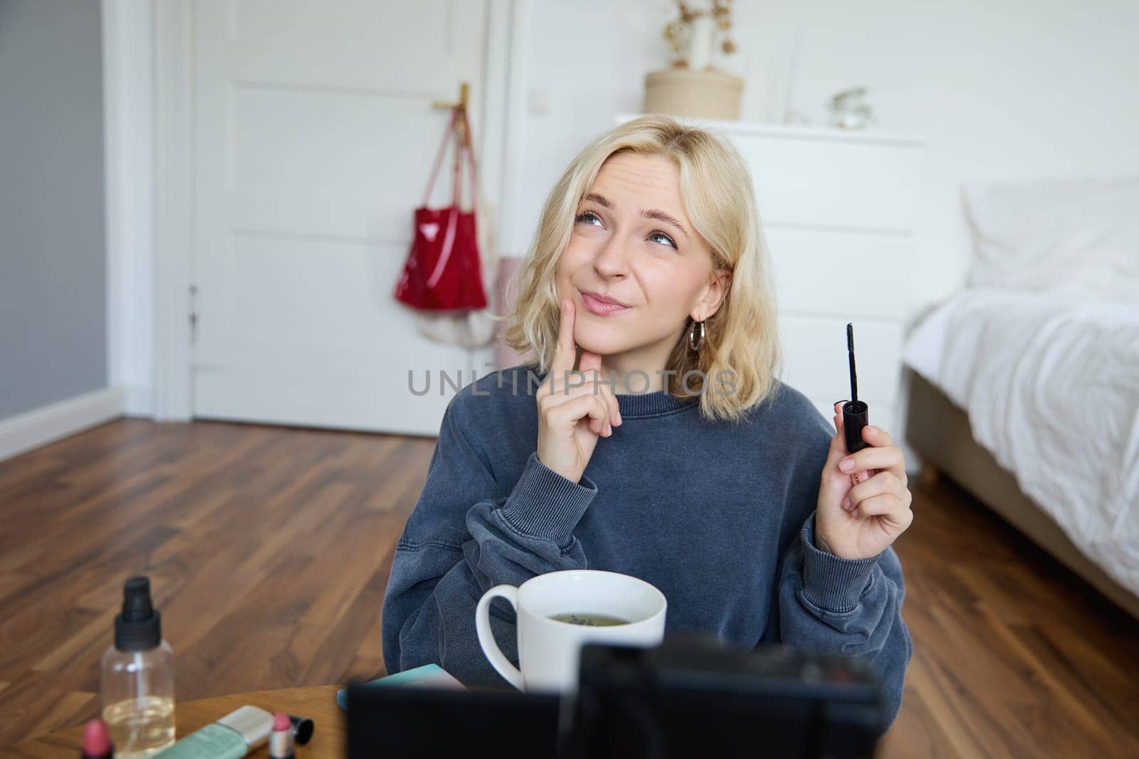 Portrait of young charismatic woman, girl records video while putting on makeup, reviewing beauty products for social media account, has a lifestyle blog, holding mascara.