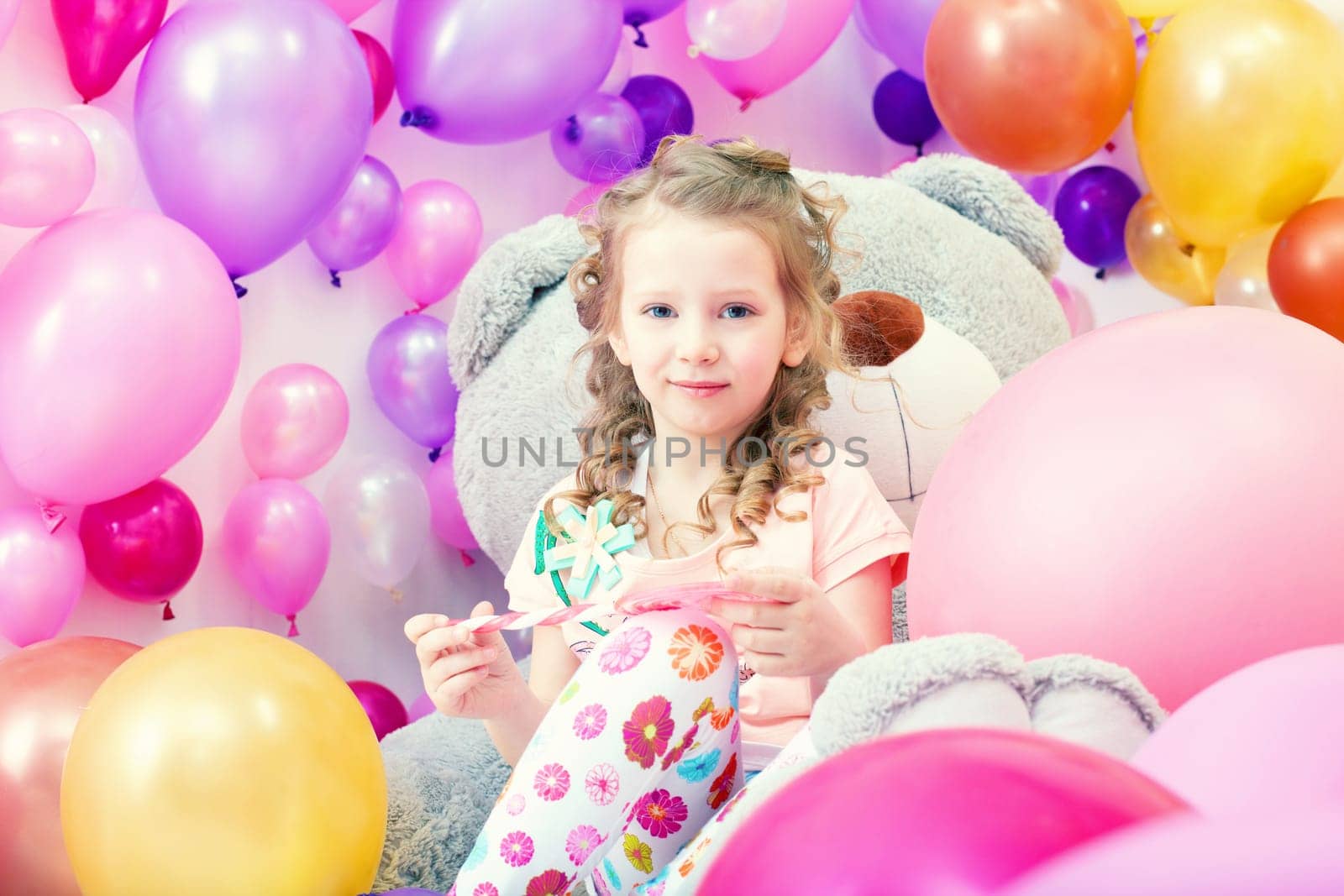 Charming curly girl playing in game room with big teddy bear