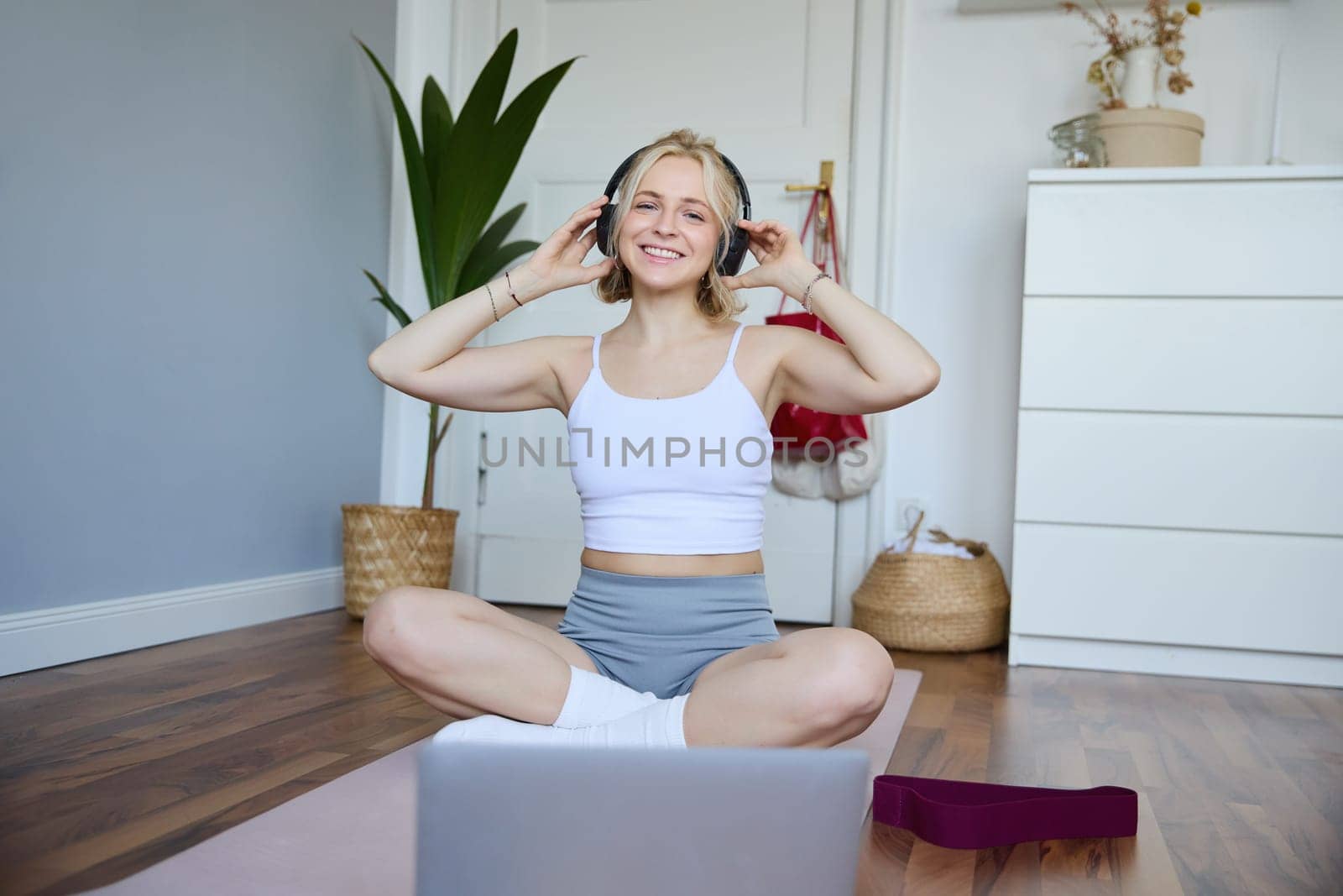 Portrait of young fitness girl, woman workout at home, listens to fitness instructor in wireless headphones, follows exercises on laptop.