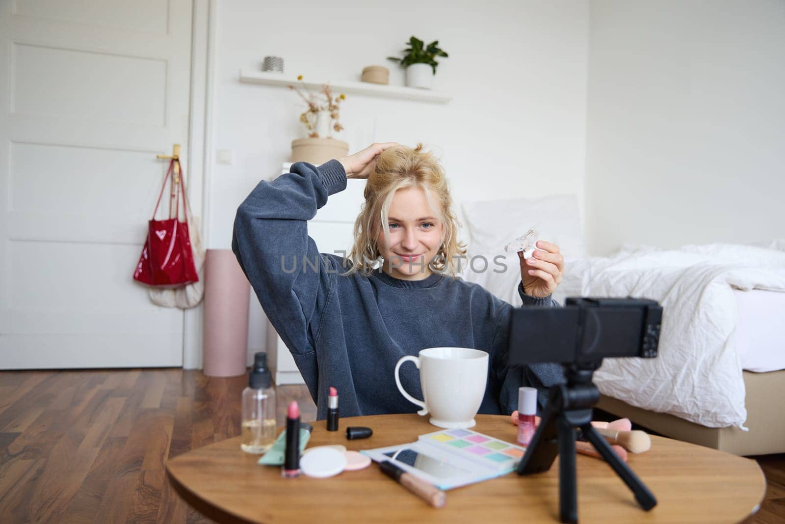 Portrait of stylish, smiling beautiful woman, recording lifestyle vlog, getting ready on camera, showing how to make her hairstyle for social media followers, vlogging from her room.