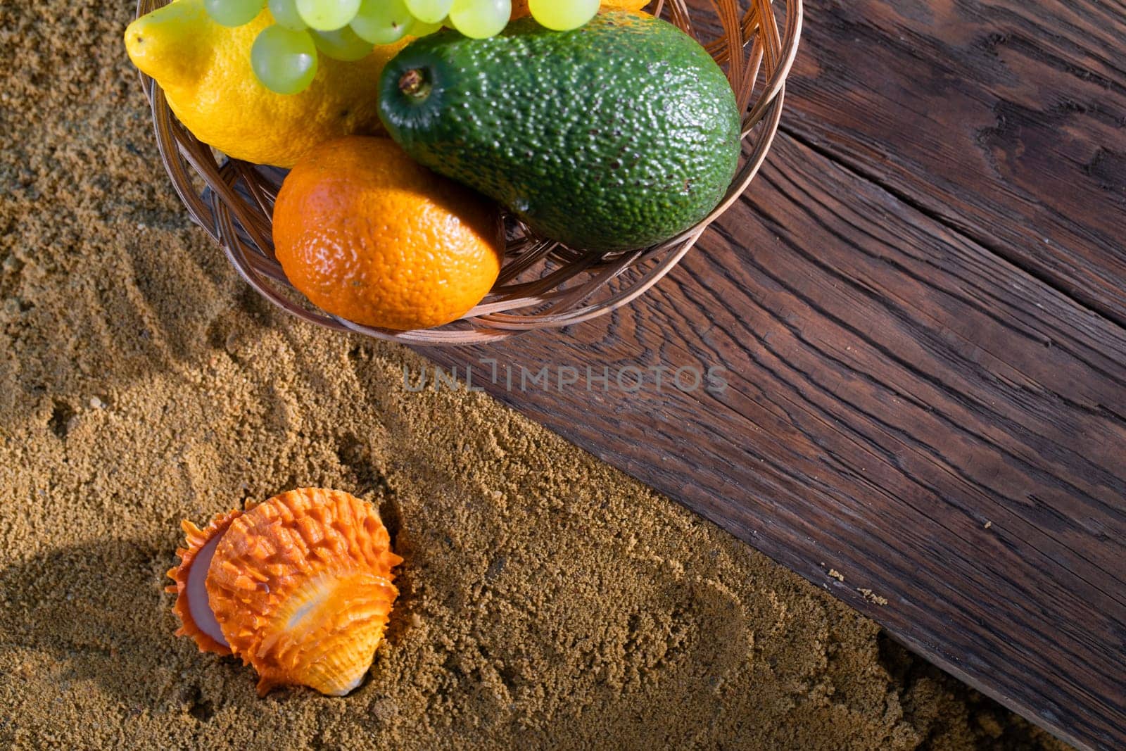 Fruit in a basket on a wooden board next to the sandy sea beach. The coast is full of wet squeak. by fotodrobik