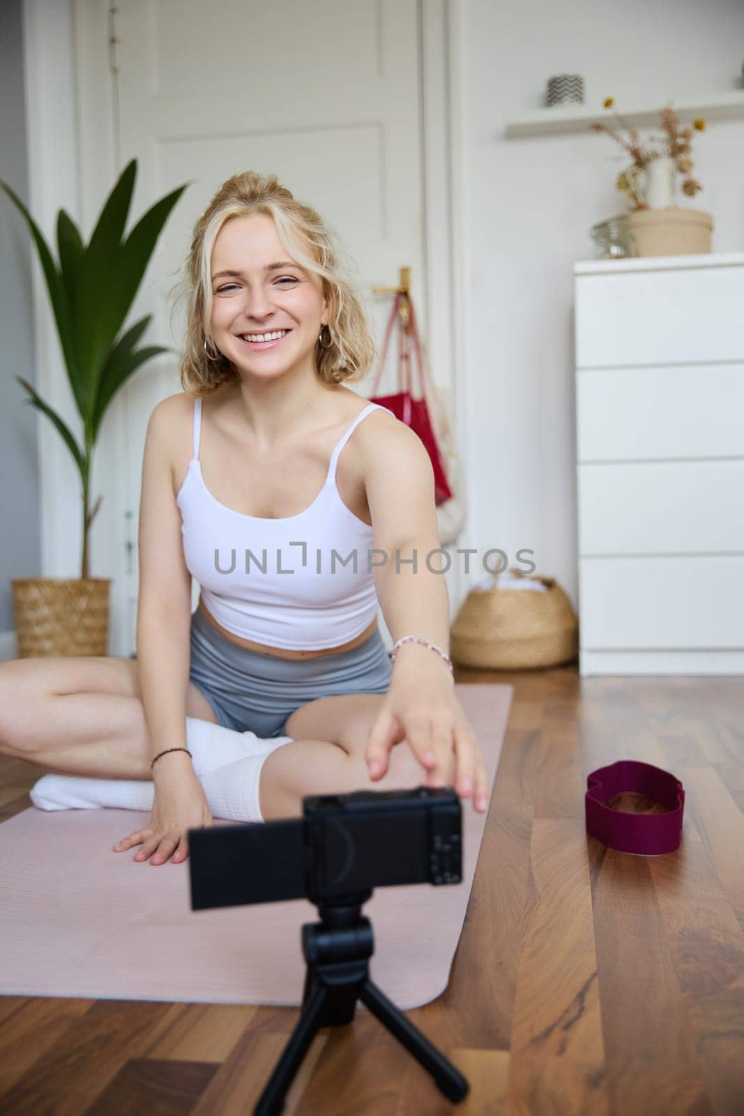 Vertical shot of smiling young woman, content creator using digital camera during workout, shooting a video vlog about fitness training and home exercises, recording her yoga.