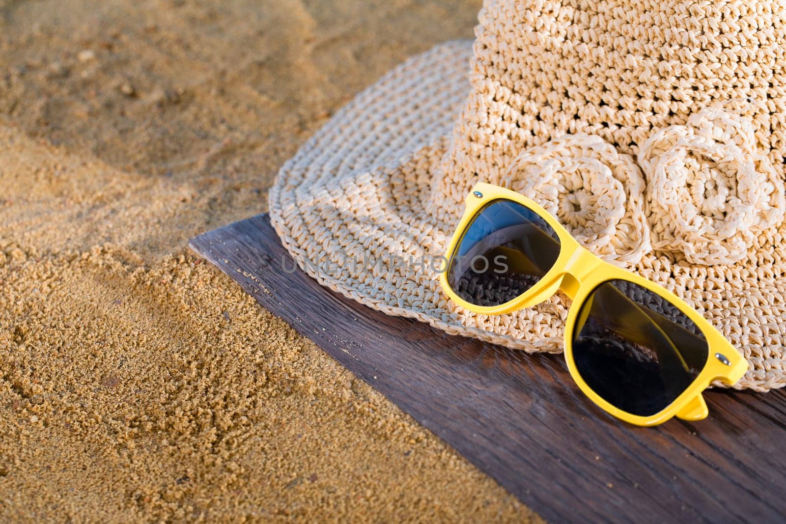 A summer hat and sunglasses lie on the sandy coast of the sea beach.